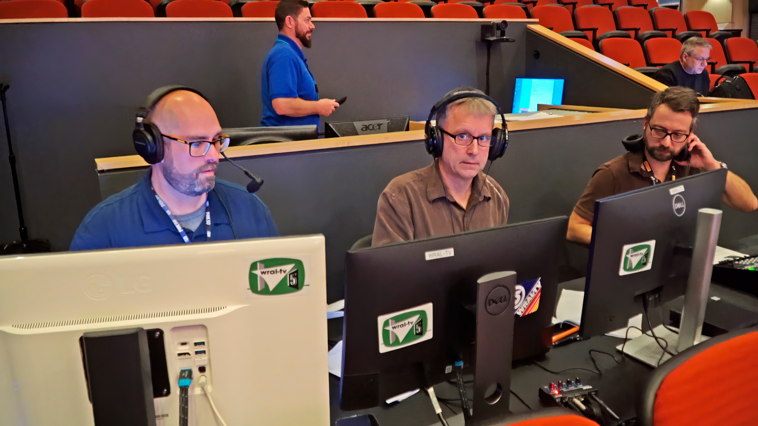 WRAL-TV production crew at their positions during taping of the Brain Game academic knowledge competition TV show in the North Campus lecture hall. Visible behind them, Wake Tech’s Jashua Cruz attends to AV system settings in the AV control booth. Photo courtesy of WRAL-TV/Capitol Broadcasting Company.