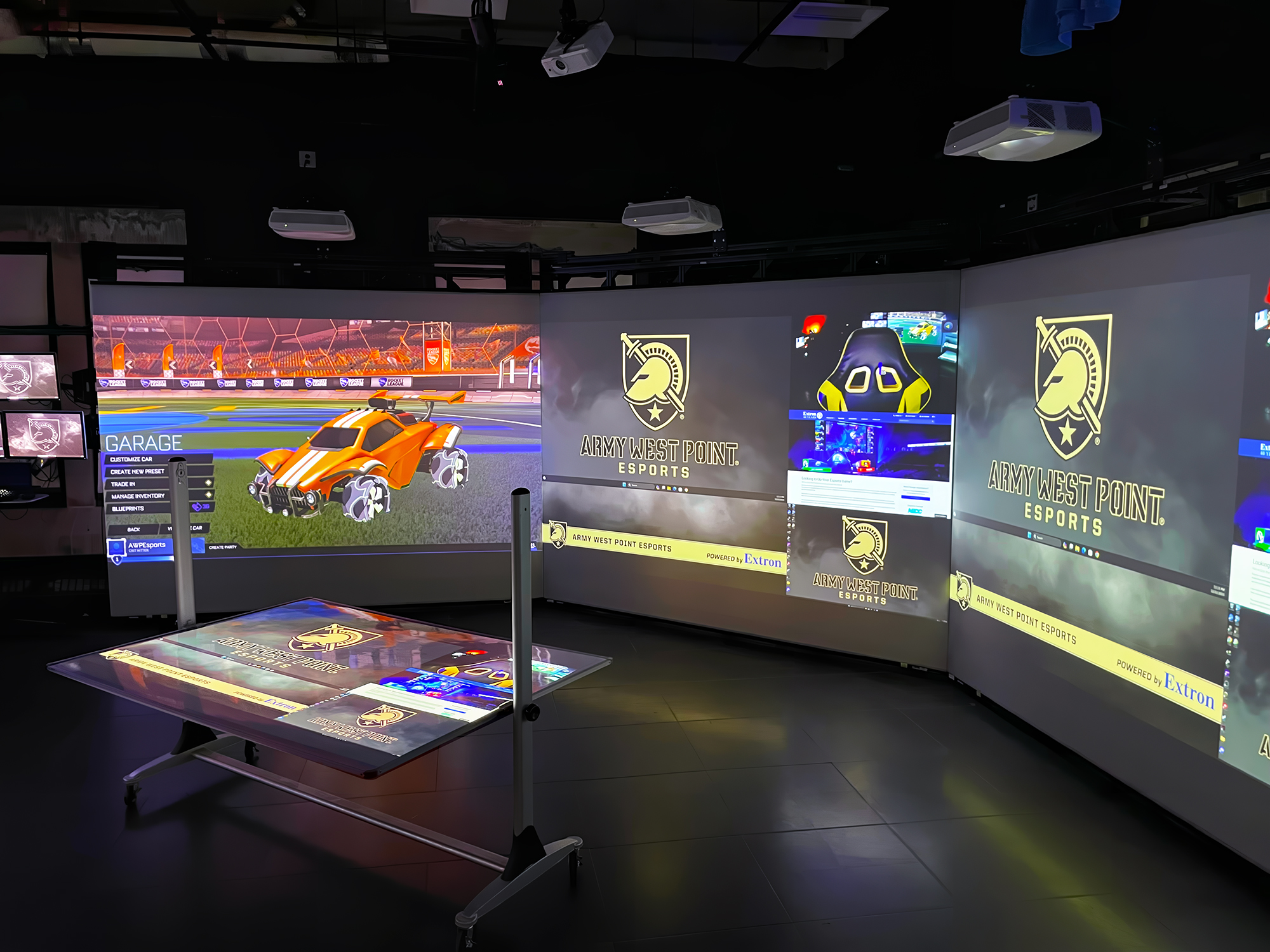 Three projection screens show gameplay action and related video content in the Immersive Display Area. A mobile whiteboard displays video from a ceiling mounted projector that points down. During strategy and coaching sessions, dry erase markers are used to annotate the projected images on the whiteboard.