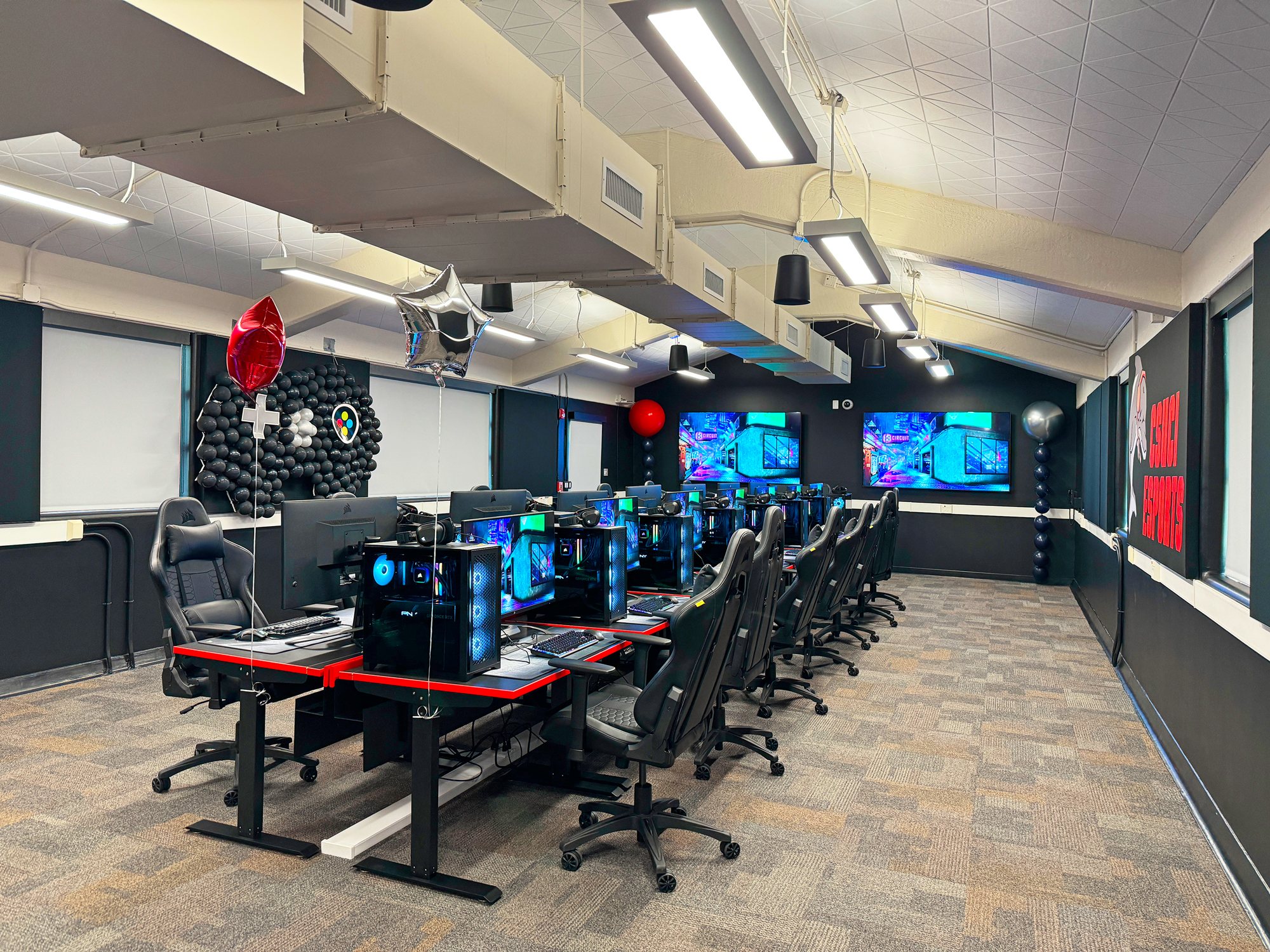 Two 75" displays are at the front of the esports lounge at the head of the long table. Seven gaming stations are on each side of the table. The instructor station is at the head of the table.