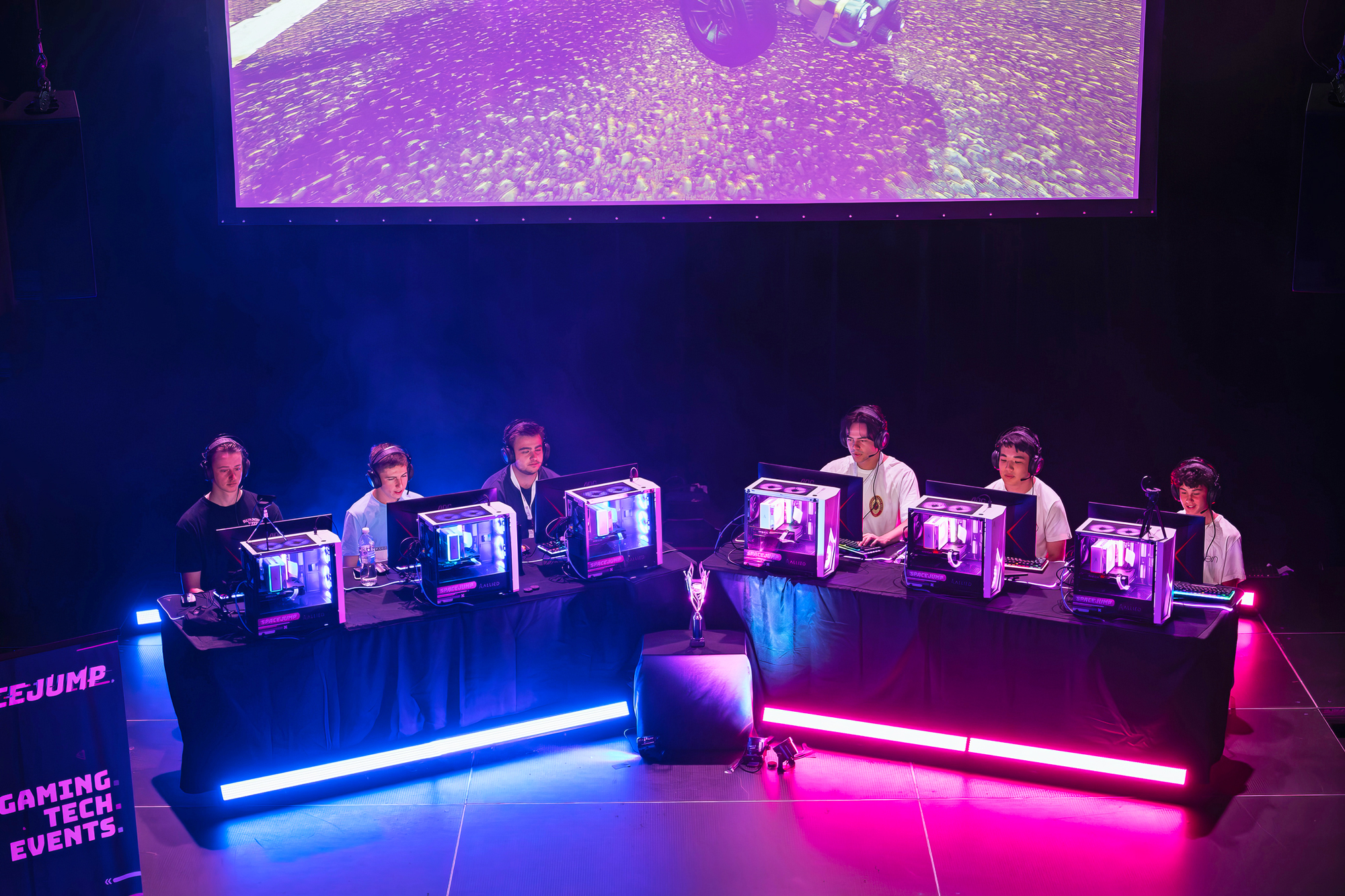 Two teams of players on the main stage focused on their gaming monitors while spectators watched the action on a large screen above the players’ heads.