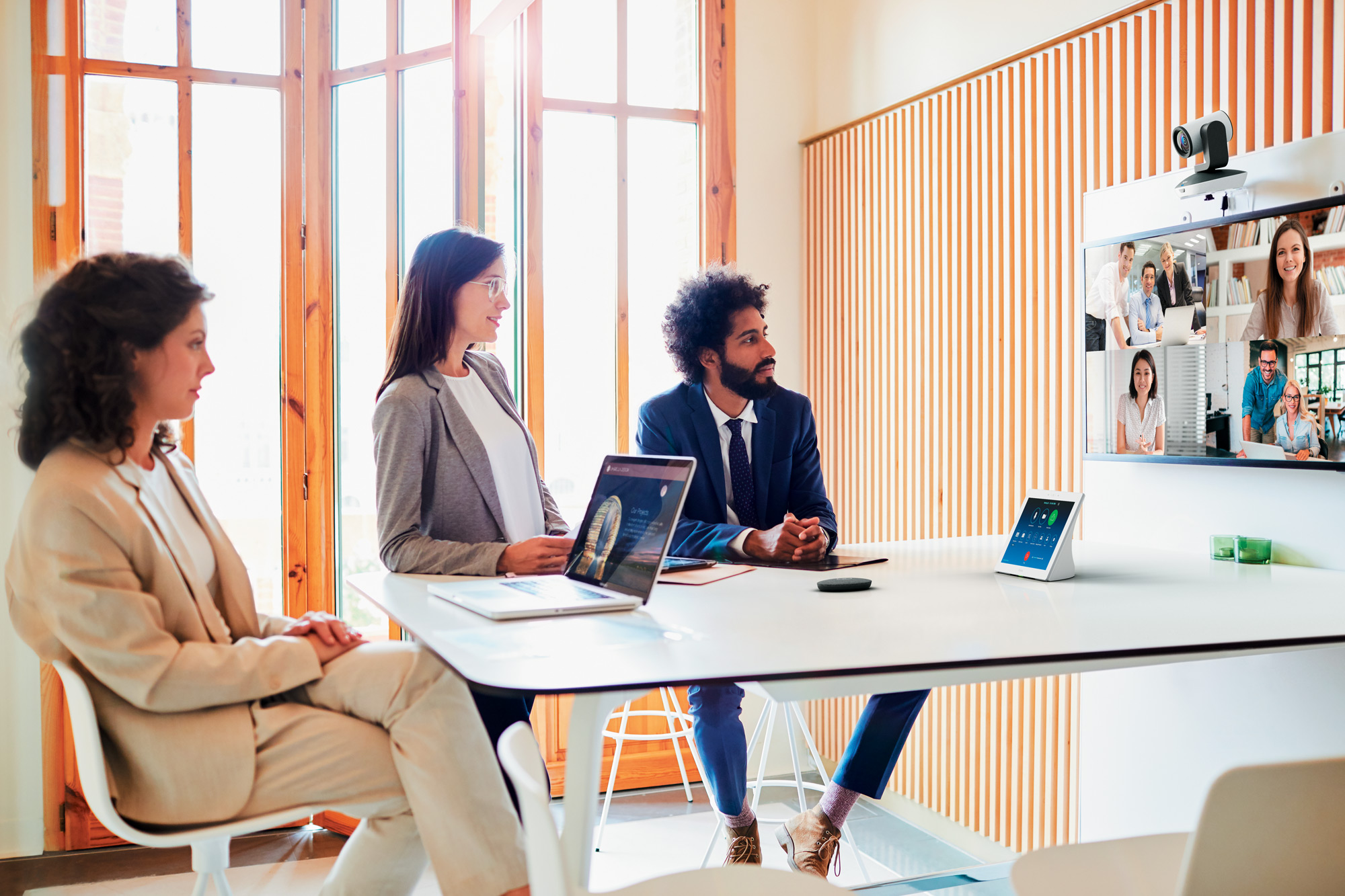 Three people in a conference room collaborating over a video call of four.