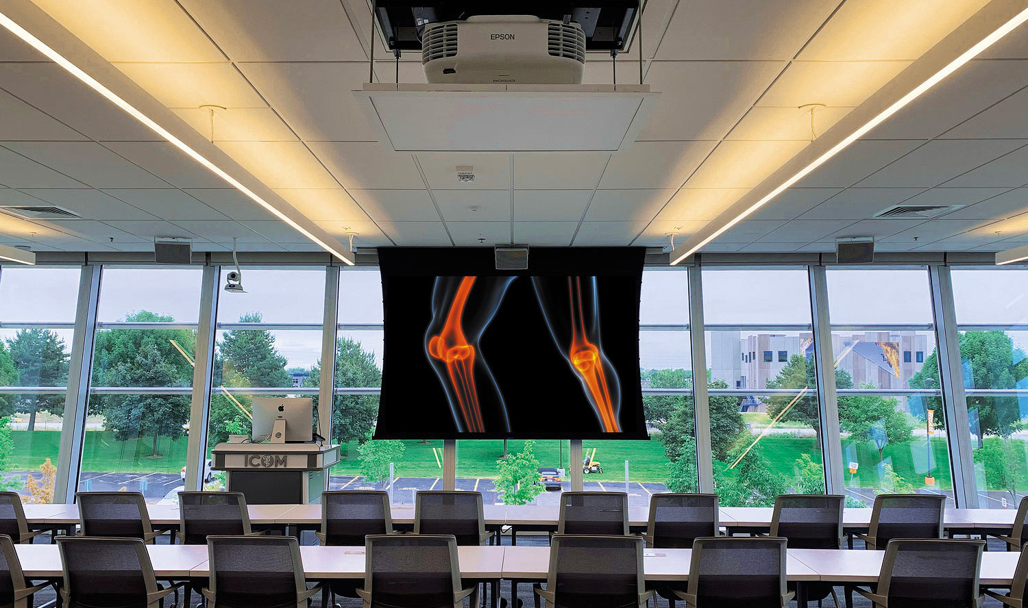 A glass walled classroom with a projector and screen at a chiropractic school.